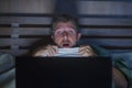 Young scared and stressed man in bed watching internet horror movie late night with laptop computer or bedroom television in