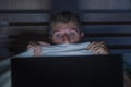 Young scared and stressed man in bed watching internet horror movie late night with laptop computer or bedroom television in Royalty Free Stock Photo