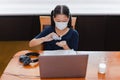 Young school girl in protective mask cleaning hands with alcohol gel while working on computer at home. Royalty Free Stock Photo