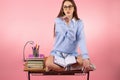 Young school girl sitting on the table with crossed legs and opened books wearing glasses for reading sends air kiss. Royalty Free Stock Photo