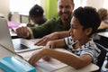 Young school teacher helping boy with study on laptop in classroom