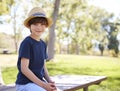 Young schoolboy in hat sits on park bench smiling to camera Royalty Free Stock Photo