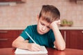 Young schoolboy learn hard at homework sitting by table and writing in notebook Royalty Free Stock Photo