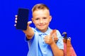 Young schoolboy wears blue t shirt holds phone striped red backpack isolated on blue background Royalty Free Stock Photo