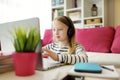 Young schoolgirl doing her homework with digital tablet at home. Child using gadgets to study. Education and distance learning for Royalty Free Stock Photo