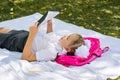 A young schoolgirl is doing homework lying on a blanket and a backpack in a sunny autumn park. Outdoor education for children. Royalty Free Stock Photo