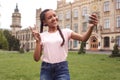 Young schoolgirl standing at school yard taking selfie on smartphone showing peace sign smiling cheerful Royalty Free Stock Photo