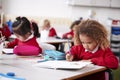 Young schoolgirl wearing school uniform sitting at a desk in an infant school classroom drawing, close up