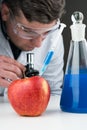 Young scientist using blue liquid, apple, syringe and microscope