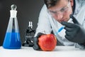 Young scientist using blue liquid, apple, syringe and microscope