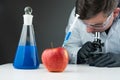 Young scientist using blue liquid, apple, syringe and microscope Royalty Free Stock Photo