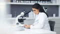 Young scientist using a digital tablet and microscope in a lab. Female pathologist analyzing medical samples while doing