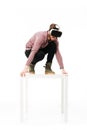 Young screaming man standing on white table in studio while playing with virtual reality glasses on white background Royalty Free Stock Photo