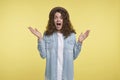 Young screaming and surprised brunette woman with curly hair and hat, happy about new present, isolated over yellow