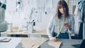 Young seamstress is checking clothing paper patterns and measuring them with tape-measure while looking at smart phone Royalty Free Stock Photo