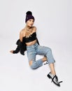 Young seductive grunge style woman in torn jeans, leather top, purple winter hat and chrome boots is sitting on floor