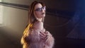 Young seductive woman, portrait in darkness. Girl in stylish pink fur coat and glasses.