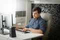 Portrait of young self-emlployed man in checkeered shirt sitting at home office and working on computer Royalty Free Stock Photo