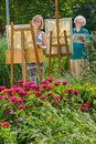 Young and senior cheerful women painting on canvas in garden during sunny day.