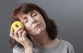 Young senior woman touching her face with golden apple for skin softness