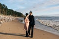 Young sensual couple having fun walking and hugging on beach. Cold autumn weather, coastline