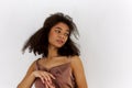 Young sensual tender curly african american woman in silk strappy dress on white looking aside