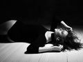 Young sensual woman in bodysuit lingerie is lying back to us on floor holding hands at her head turned. Top view. Black and white Royalty Free Stock Photo