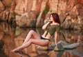 Young sensual woman sitting pensively on stones of lake on the background of rocky mountains Royalty Free Stock Photo