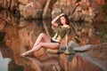 Young sensual woman sitting pensively on stones of lake on the background of rocky mountains Royalty Free Stock Photo