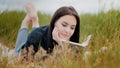 Young serene caucasian brunet woman girl lying on grass outdoors attractive smiling teenage student reads book enjoy Royalty Free Stock Photo