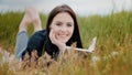 Young serene caucasian brunet woman girl lying on grass outdoors attractive smiling teenage student reads book enjoy Royalty Free Stock Photo