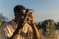 Young serene male photographer-amateur snapping photos of the impressive view of a calm river under the blazing evening