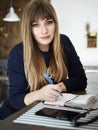 Young serious attractive young woman with pen in hand thinking on plans and writing list to do in notepad enjoying Royalty Free Stock Photo