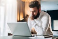 Young serious bearded businessman standing in office near table and using laptop. Man works on computer, checks e-mail Royalty Free Stock Photo