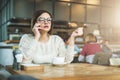 Young serious businesswoman in glasses sitting in cafe at wooden table and talking on cell phone. Royalty Free Stock Photo