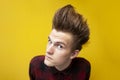 Serious guy with a funny hairstyle looks at the camera closely on a yellow isolated background, a man suspects