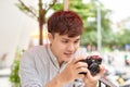 Young serious male sitting at wooden table with photo camera and preparing for photo session while having coffee break Royalty Free Stock Photo