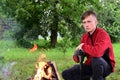 young serious man with an axe by fire in forest. Time for rest. Take a break. The path to nature. Royalty Free Stock Photo