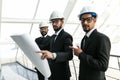 Young serious indian man in helmet and tie with tablet escorted with two engineers and pointing at building pipes. Controller Royalty Free Stock Photo