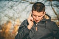 Young serious man holding mobile phone, using smartphone, making a call, talking on the phone, standing on sunny street Royalty Free Stock Photo