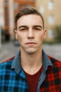 Young serious man with a stylish hairstyle in a fashionable t-shirt in a trendy plaid shirt walks around the city