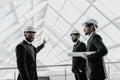 Young serious indian man in helmet and tie with tablet escorted with two engineers and pointing at building pipes. Controller Royalty Free Stock Photo
