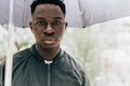 Young African man under black umbrella in rain, sad. Fall or spring weather Royalty Free Stock Photo