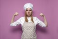 Serious strong girl cook in apron shows strength on a pink background, woman housewife in kitchen clothes Royalty Free Stock Photo