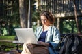 A young serious woman student sitting on a bench in the park and typing on her laptop on a sunny day in universiry campus Royalty Free Stock Photo