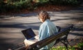 A young serious woman student sitting on a bench in the park and typing on her laptop on a sunny day in universiry campus Royalty Free Stock Photo