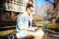 A young serious woman student sitting on a bench in the park and typing on her laptop on a sunny day in universiry campus Royalty Free Stock Photo