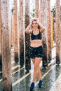 Young sexy athlete woman wearing black sport bra and shorts staying under drops of the water after training session in the morning