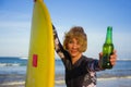 Young beautiful and happy surfer woman holding yellow surf board smiling cheerful drinking beer bottle enjoying summer holida Royalty Free Stock Photo