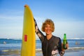 Young beautiful and happy surfer woman holding yellow surf board smiling cheerful drinking beer bottle enjoying summer holida Royalty Free Stock Photo